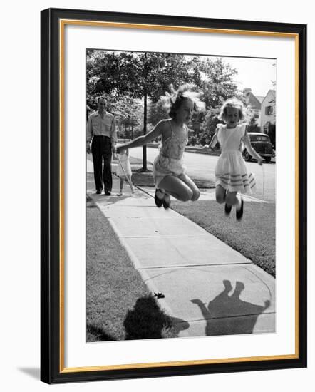 Girls on the street in neighborhood using rope to jump in tandem while man with toddler watches-Alfred Eisenstaedt-Framed Photographic Print