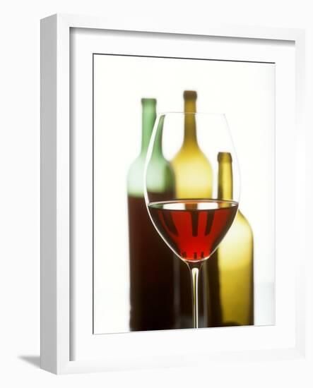 Glass of Red Wine in Front of Three Wine Bottles-Joerg Lehmann-Framed Photographic Print