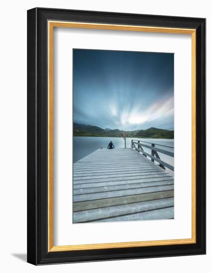 Hiker on wooden deck admires the sea illuminated by blue lights at night, Holdalsvatnet, Vestvagoy,-Roberto Moiola-Framed Photographic Print