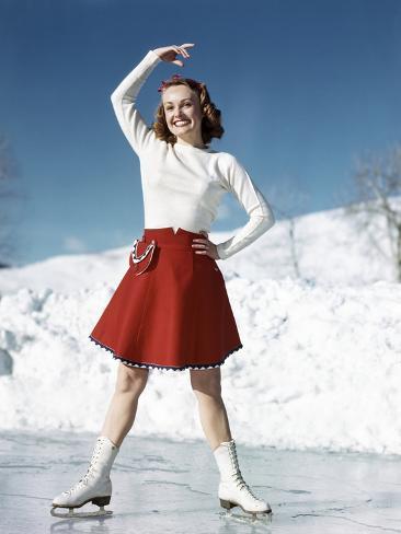Photographic Print: 1950s SMILING WOMAN WEARING WHITE SWEATER RED SKIRT ICE SKATING POSING WITH ARM OVER HEAD by Panoramic Images: 12x9in