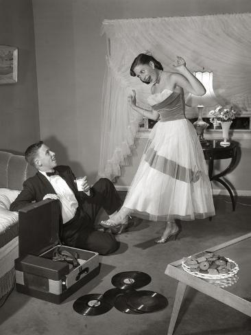 Photographic Print: 1950s 1960s TEEN COUPLE IN LIVING ROOM IN PROM DRESS & TUXEDO GUY SITTING ON FLOOR & GIRL DANCIN. by Panoramic Images: 12x9in