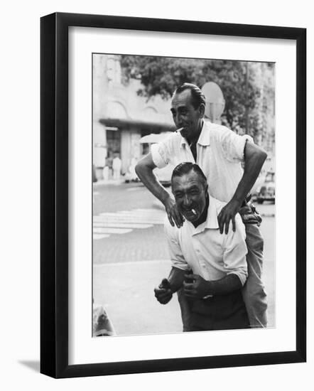 Italian Man Leaping Onto a Friend's Back in Casual Greeting While Crossing a Piazza-Paul Schutzer-Framed Photographic Print