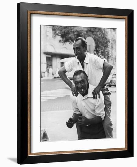 Italian Man Leaping Onto a Friend's Back in Casual Greeting While Crossing a Piazza-Paul Schutzer-Framed Photographic Print