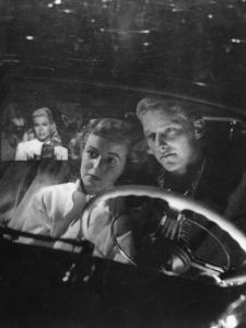 Young Couple Snuggling in Convertible as They Intently Watch Movie at Drive-in Movie Theater by J^ R^ Eyerman