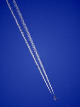 jumbo jet airliner races across a clear blue sky with vapor trails vapor trails
