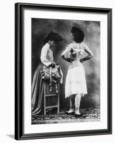 Lady Tries on a Corset While Another Woman Waits with Another One-null-Framed Photographic Print