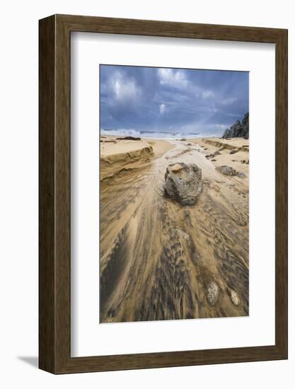 Low angle of a stream flowing around a rock heading into the ocean with stormy skies and a rainbow-Sheila Haddad-Framed Photographic Print