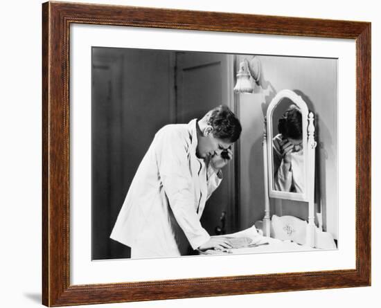 Man Bending over a Piece of Paper on His Dresser and Holding His Head-null-Framed Photo