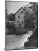 Man Fishing Beside a Waterfall and a 100 Year Old Mill-Bob Landry-Mounted Photographic Print