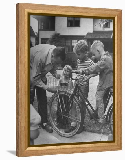 Man Fixing Basket on Bicycle as Children Watch Attentively-Nina Leen-Framed Premier Image Canvas