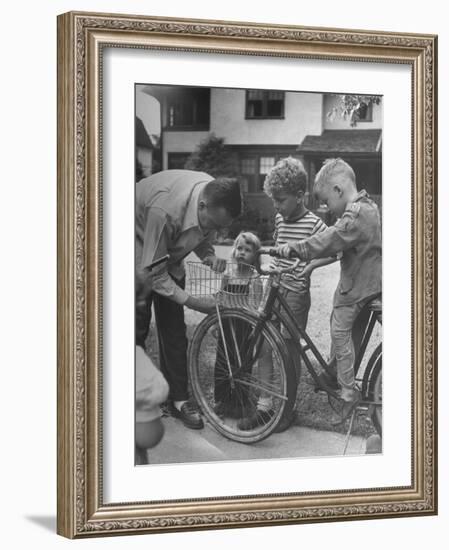 Man Fixing Basket on Bicycle as Children Watch Attentively-Nina Leen-Framed Photographic Print