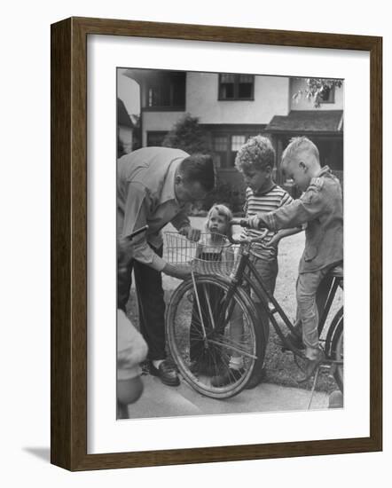 Man Fixing Basket on Bicycle as Children Watch Attentively-Nina Leen-Framed Photographic Print