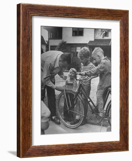 Man Fixing Basket on Bicycle as Children Watch Attentively-Nina Leen-Framed Photographic Print