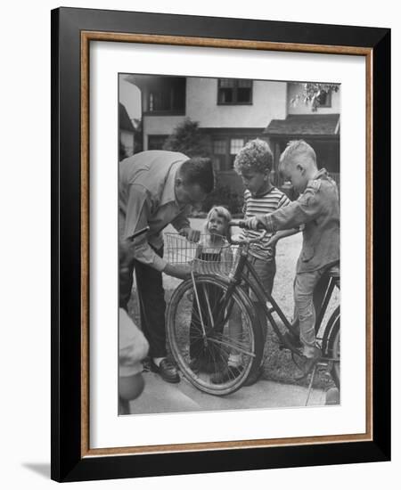 Man Fixing Basket on Bicycle as Children Watch Attentively-Nina Leen-Framed Photographic Print