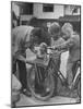 Man Fixing Basket on Bicycle as Children Watch Attentively-Nina Leen-Mounted Photographic Print