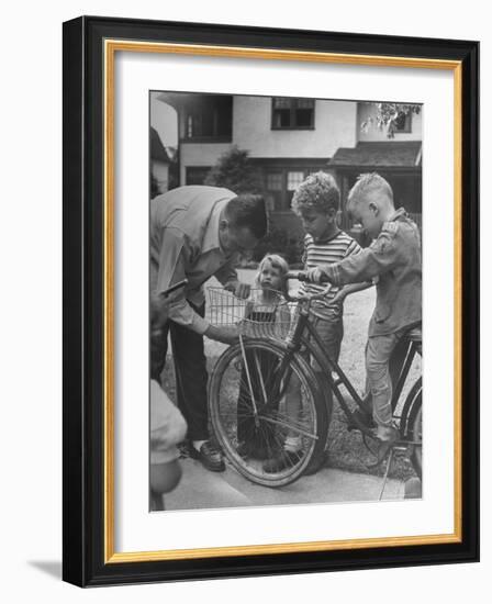 Man Fixing Basket on Bicycle as Children Watch Attentively-Nina Leen-Framed Photographic Print