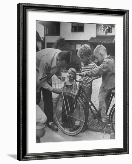 Man Fixing Basket on Bicycle as Children Watch Attentively-Nina Leen-Framed Photographic Print