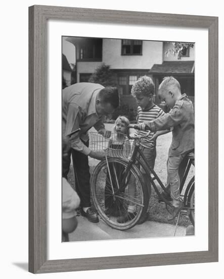 Man Fixing Basket on Bicycle as Children Watch Attentively-Nina Leen-Framed Photographic Print