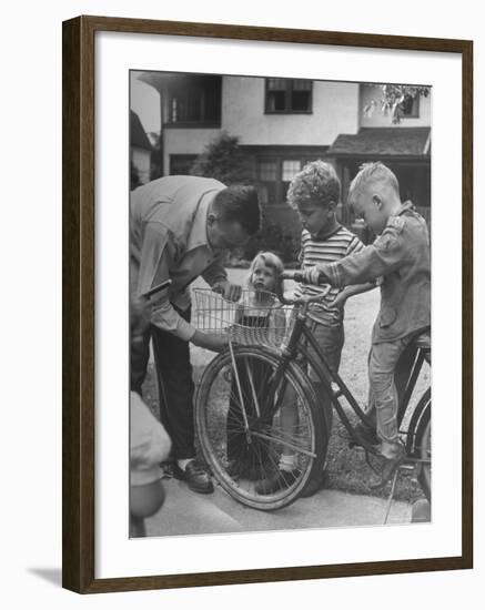 Man Fixing Basket on Bicycle as Children Watch Attentively-Nina Leen-Framed Photographic Print