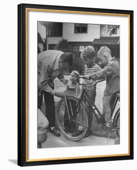 Man Fixing Basket on Bicycle as Children Watch Attentively-Nina Leen-Framed Photographic Print