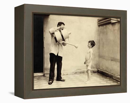 Man Is Sprinkling Boy with Water from Watering Can, 20th Century-Andrew Pitcairn-knowles-Framed Premier Image Canvas