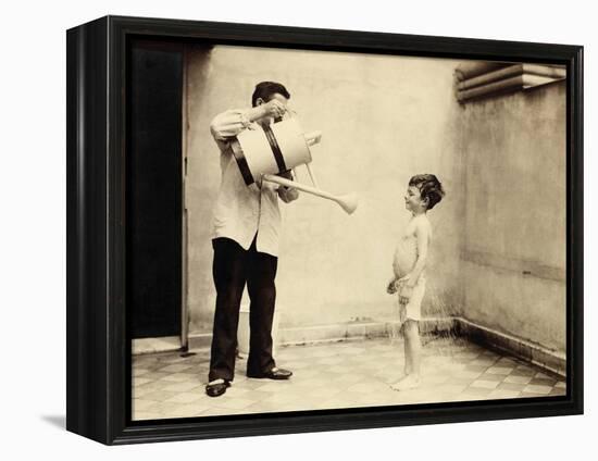 Man Is Sprinkling Boy with Water from Watering Can, 20th Century-Andrew Pitcairn-knowles-Framed Premier Image Canvas