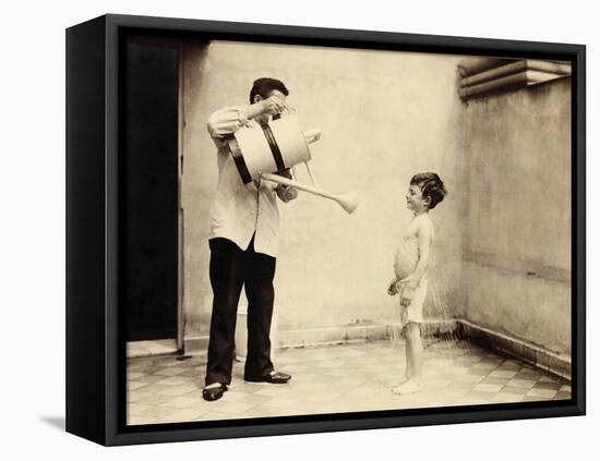 Man Is Sprinkling Boy with Water from Watering Can, 20th Century-Andrew Pitcairn-knowles-Framed Premier Image Canvas