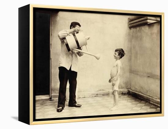 Man Is Sprinkling Boy with Water from Watering Can, 20th Century-Andrew Pitcairn-knowles-Framed Premier Image Canvas