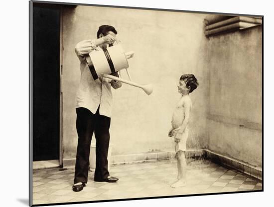 Man Is Sprinkling Boy with Water from Watering Can, 20th Century-Andrew Pitcairn-knowles-Mounted Giclee Print