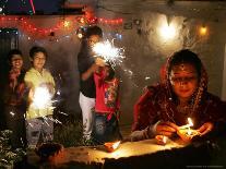 A Woman Lights Earthen Lamps as Children Ignite Firecrackers in New Delhi-Manish Swarup-Photographic Print