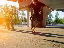 Silhouette Skateboarder Jumping in City on Skateboard under the Bridge. in the Background Two Young-Maxim Blinkov-Photographic Print