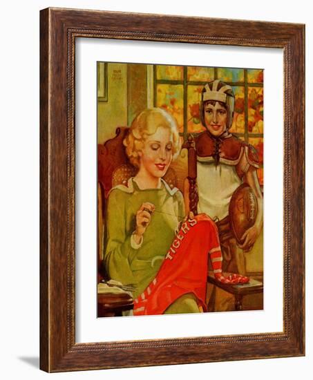 Mother Sews Her Son's Football Jersey As He Looks On-null-Framed Art Print