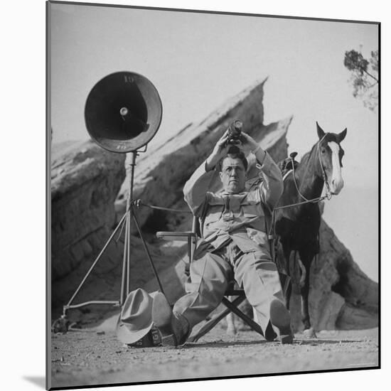 Movie Director George Stevens Holding Up a Rangefinder as He Directs Scene for the Movie "Giant"-Allan Grant-Mounted Premium Photographic Print