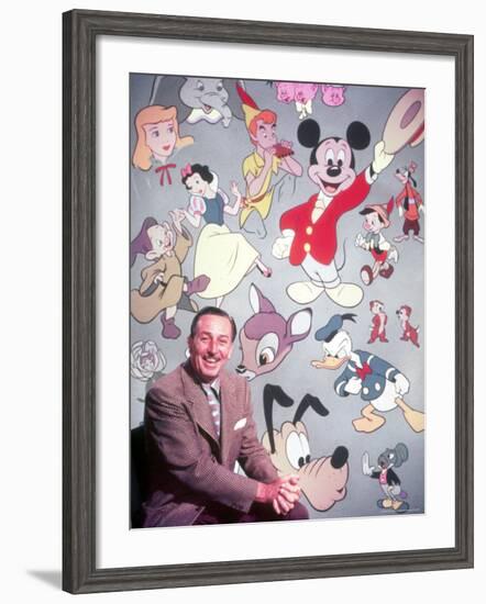 Movie Studio Head Walt Disney Sitting in Front of Backdrop Filled with Disney Creations-Alfred Eisenstaedt-Framed Premium Photographic Print