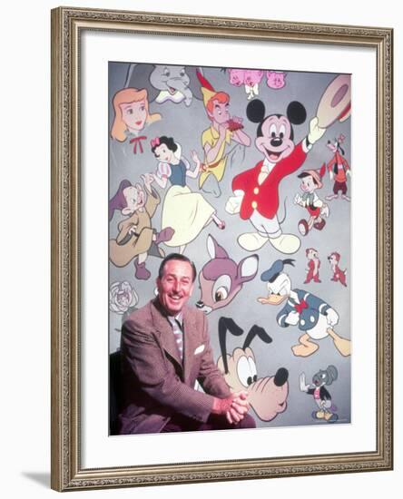 Movie Studio Head Walt Disney Sitting in Front of Backdrop Filled with Disney Creations-Alfred Eisenstaedt-Framed Premium Photographic Print