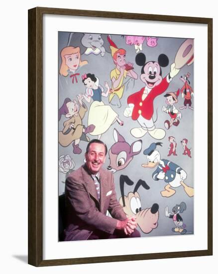 Movie Studio Head Walt Disney Sitting in Front of Backdrop Filled with Disney Creations-Alfred Eisenstaedt-Framed Premium Photographic Print