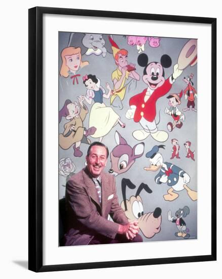 Movie Studio Head Walt Disney Sitting in Front of Backdrop Filled with Disney Creations-Alfred Eisenstaedt-Framed Premium Photographic Print