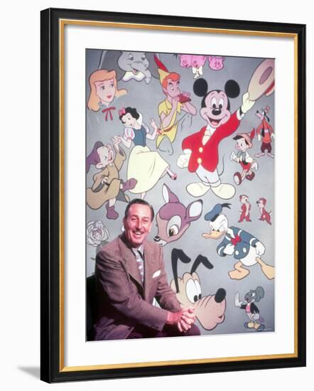 Movie Studio Head Walt Disney Sitting in Front of Backdrop Filled with Disney Creations-Alfred Eisenstaedt-Framed Premium Photographic Print