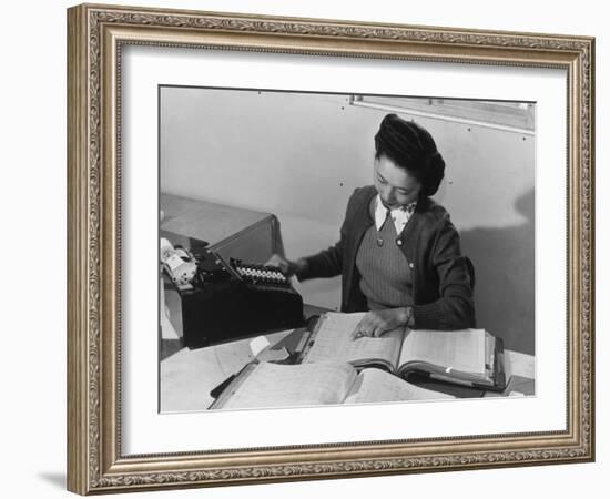 Mrs Teruko Kiyomura, bookkeeper, seated at desk, operating an adding machine while reading a ledger-Ansel Adams-Framed Photographic Print