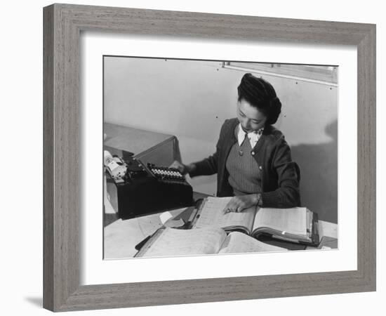 Mrs Teruko Kiyomura, bookkeeper, seated at desk, operating an adding machine while reading a ledger-Ansel Adams-Framed Photographic Print