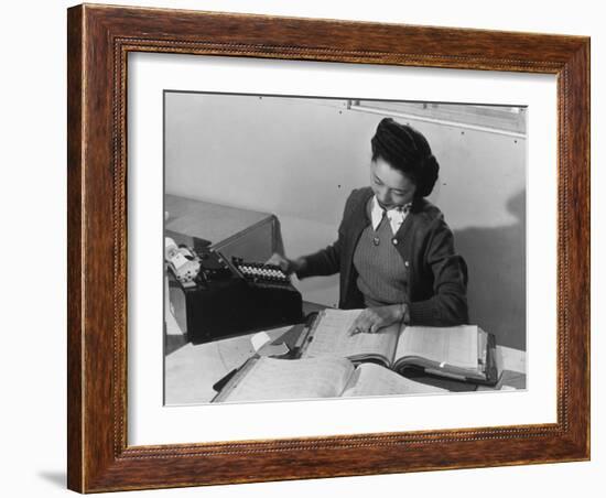 Mrs Teruko Kiyomura, bookkeeper, seated at desk, operating an adding machine while reading a ledger-Ansel Adams-Framed Photographic Print