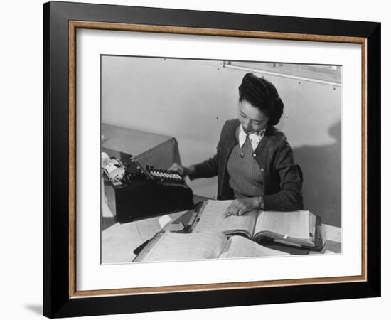 Mrs Teruko Kiyomura, bookkeeper, seated at desk, operating an adding machine while reading a ledger-Ansel Adams-Framed Photographic Print