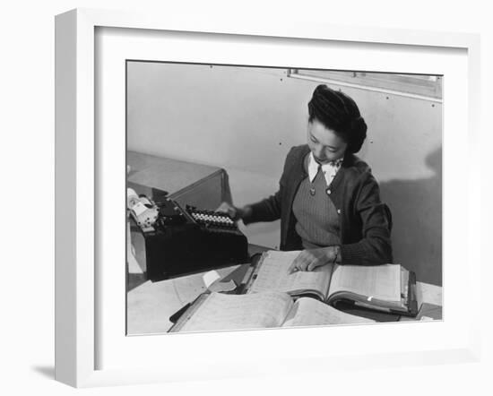 Mrs Teruko Kiyomura, bookkeeper, seated at desk, operating an adding machine while reading a ledger-Ansel Adams-Framed Photographic Print