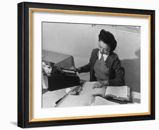 Mrs Teruko Kiyomura, bookkeeper, seated at desk, operating an adding machine while reading a ledger-Ansel Adams-Framed Photographic Print