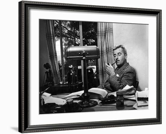 Novelist and Script Writer William Faulkner Smoking a Pipe at His Desk at Warner Brothers Studios-null-Framed Premium Photographic Print