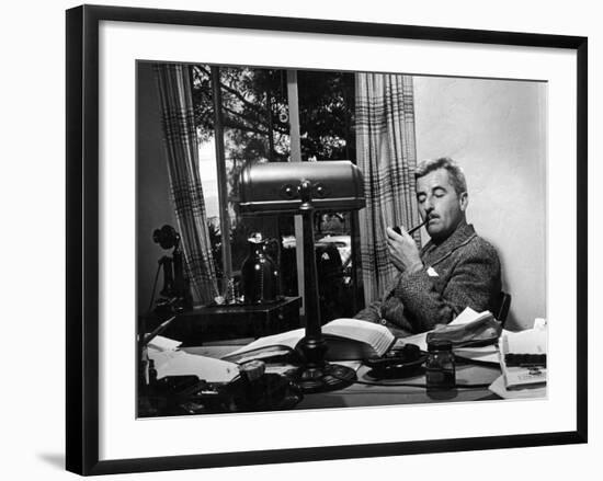 Novelist and Script Writer William Faulkner Smoking a Pipe at His Desk at Warner Brothers Studios-null-Framed Premium Photographic Print