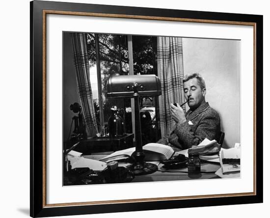 Novelist and Script Writer William Faulkner Smoking a Pipe at His Desk at Warner Brothers Studios-null-Framed Premium Photographic Print