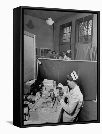Nurse Sitting at Table with Medical Supplies While Doctors Examine Patient in Background-Wallace Kirkland-Framed Premier Image Canvas