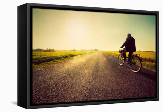 Old Man Riding A Bike On Asphalt Road Towards The Sunny Sunset Sky-Michal Bednarek-Framed Stretched Canvas