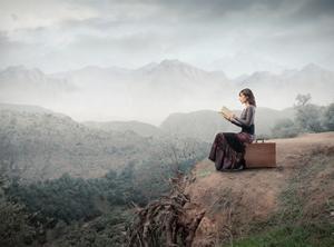 Woman Sitting On A Suitcase And Reading A Book With Landscape On The Background by olly2